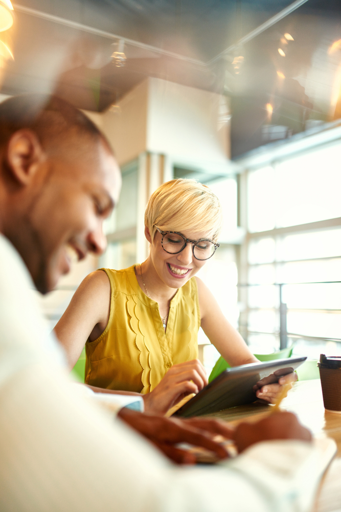 Two creative millenial small business owners working on social media strategy using a digital tablet while sitting at desk Two creative millenial small business owners working on social media strategy using a digital tablet while sitting at desk